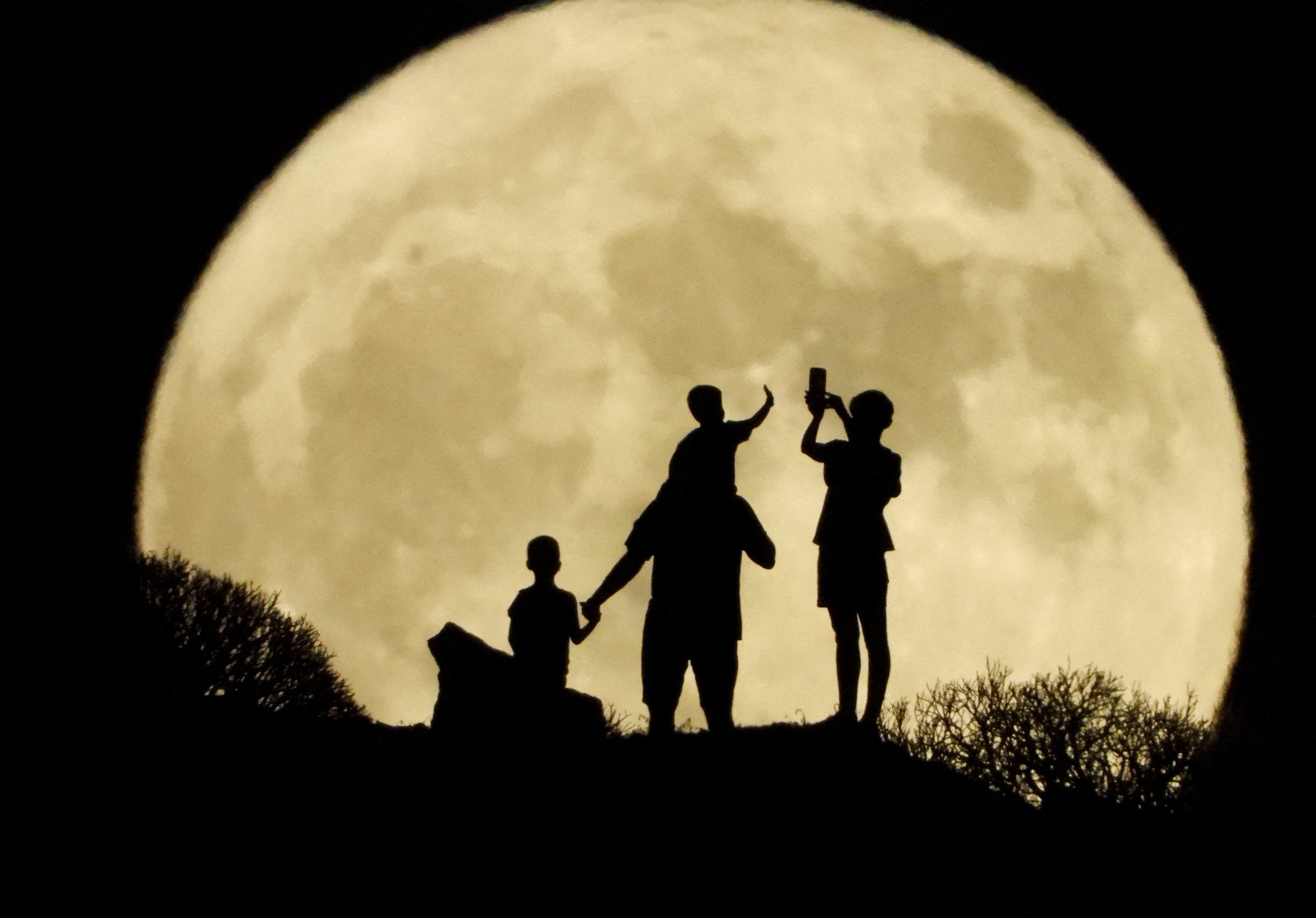 A family stand with the full moon known as the "Sturgeon Moon" in the background, in Arguineguin